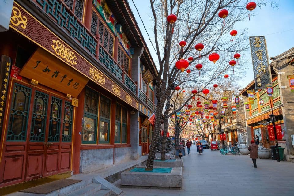 Une rue de ville est bordée de bâtiments traditionnels et d'arbres dépouillés décorés de nombreuses lanternes en papier rouges.