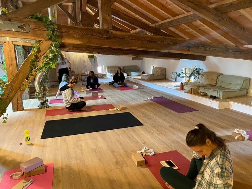 Un voyage de groupe WeRoad pratiquant le yoga dans un studio rustique sous les combles, avec un parquet en bois et des poutres apparentes.