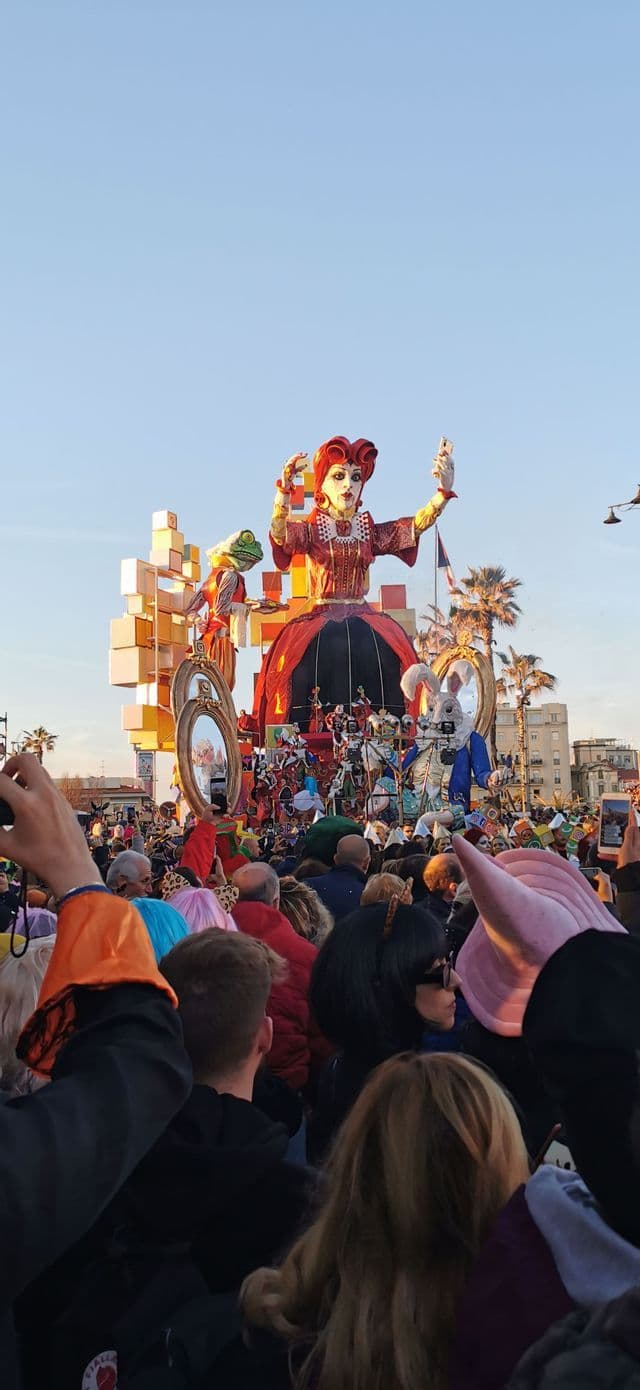 Un grande carro di carnevale con la Regina di Cuori che si scatta un selfie è ammirato da una vasta folla di spettatori.