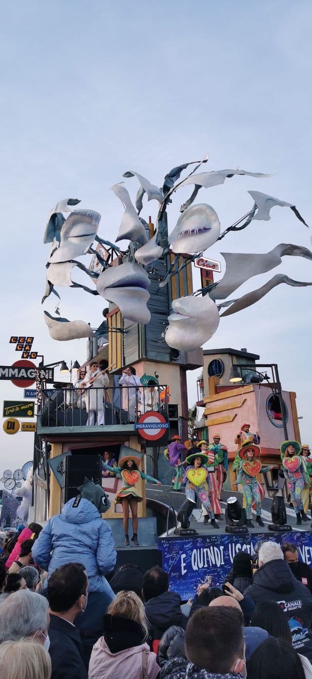 Un carro allegorico sontuoso con artisti in costumi colorati che ballano e suonano musica per una vasta folla di spettatori.