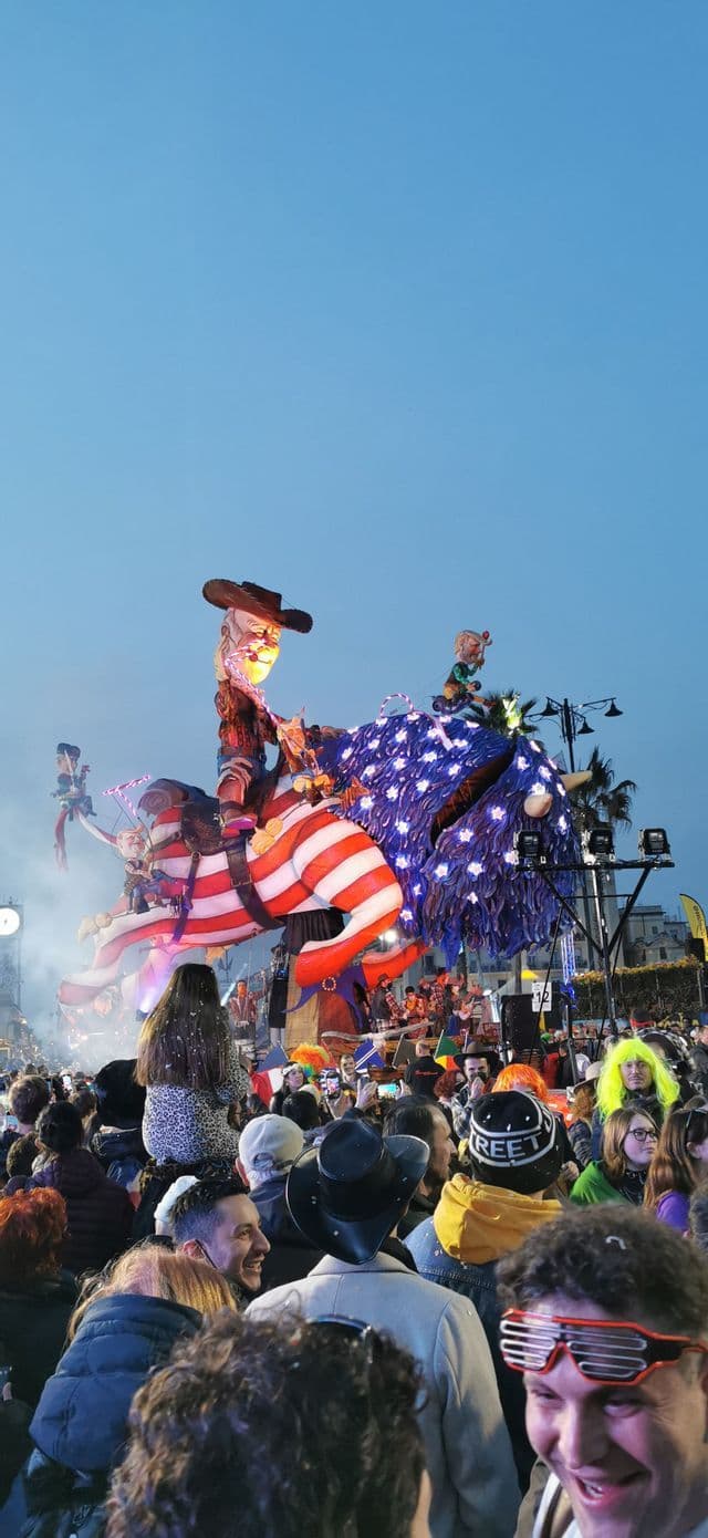 Un viaggio di gruppo WeRoad in mezzo a una grande folla che guarda una parata festiva con un elaborato carro allegorico al tramonto.