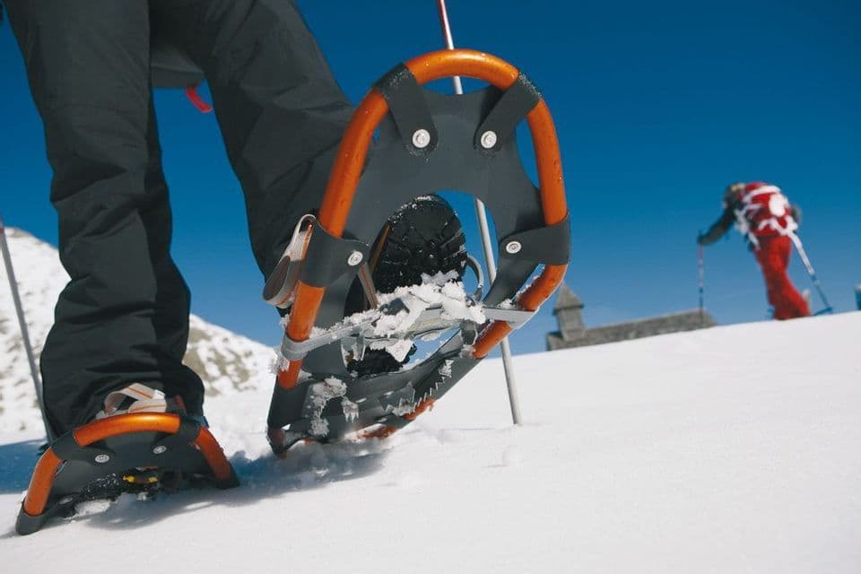 Primo piano di uno scarpone con ciaspola arancione nella neve fresca su una montagna soleggiata.