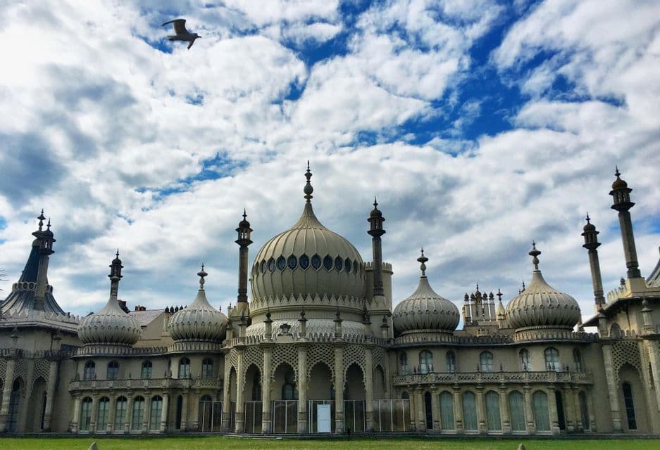Un palazzo sontuoso a cupola, con minareti, si erge su un prato verde sotto un cielo azzurro nuvoloso mentre un uccello vola sopra.