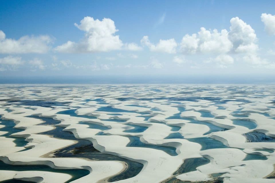 Una vista aerea di vaste dune di sabbia bianca piene di lagune di acqua blu sotto un cielo parzialmente nuvoloso.