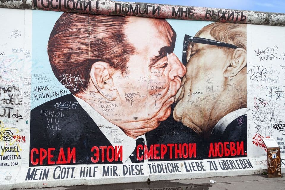 The 'Fraternal Kiss' mural by Dmitri Vrubel on the East Side Gallery section of the Berlin Wall, covered in various graffiti.