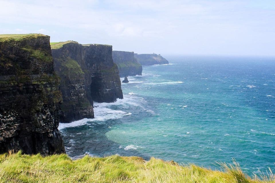 Une vue du haut d'une falaise verdoyante, face à une série de falaises rocheuses abruptes plongeant dans un océan turquoise.