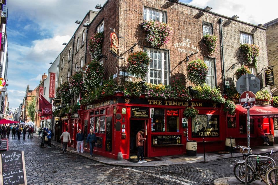 Le pub Temple Bar, avec sa façade rouge et ses fleurs suspendues, à l'angle d'une rue pavée avec des piétons qui passent.