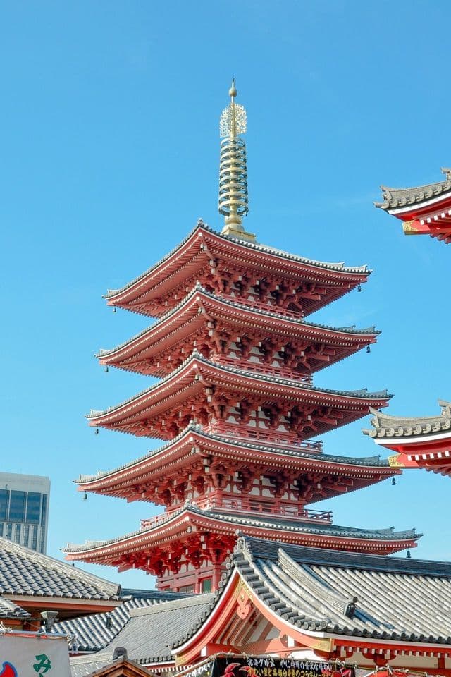 Una pagoda alta, rossa, a cinque piani con un ornato pinnacolo dorato si staglia contro un cielo limpido e azzurro brillante.