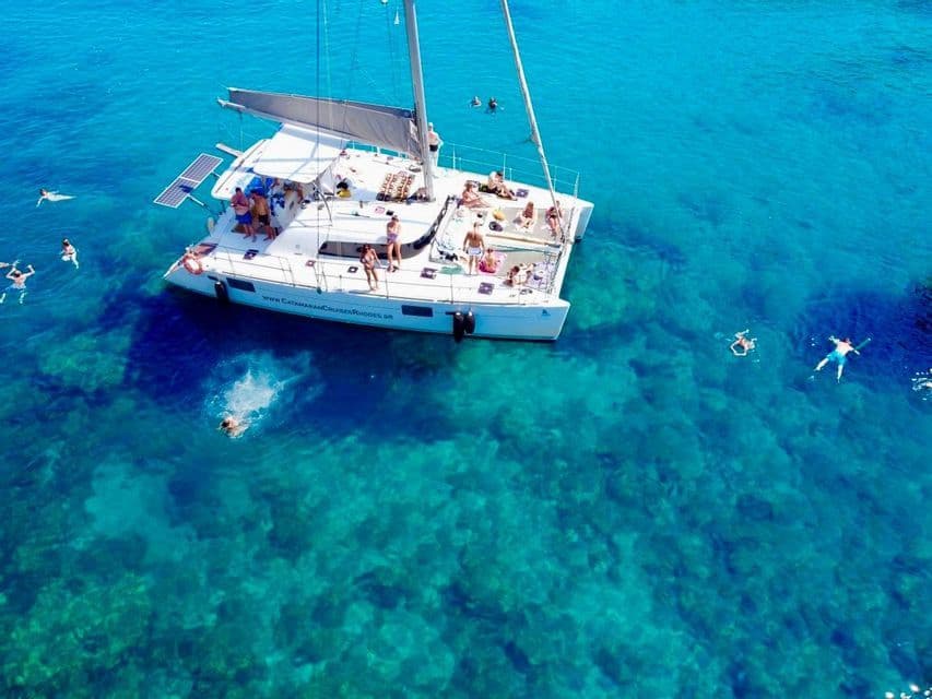 Una vista aerea di un viaggio di gruppo WeRoad su un catamarano bianco, con persone che nuotano e si tuffano nell'acqua cristallina color turchese.