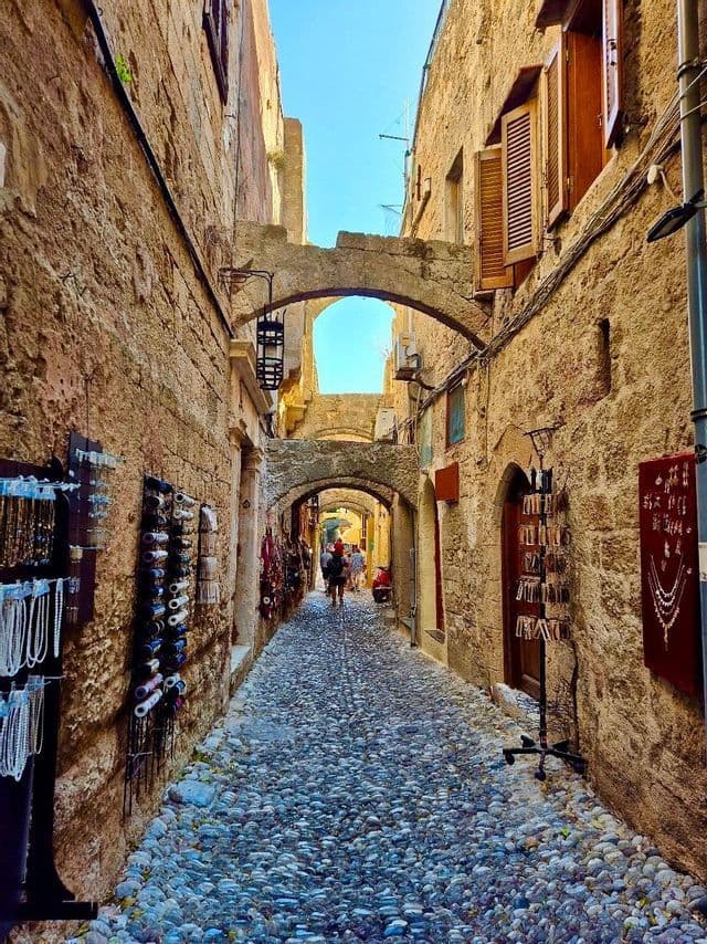 Una stretta strada acciottolata passa sotto archi di pietra tra vecchi edifici fiancheggiati da negozi di souvenir.