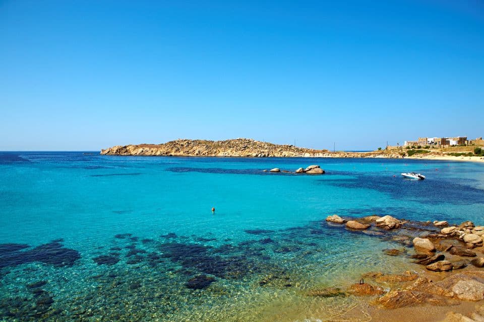 Una baia costiera con acqua cristallina turchese, una costa rocciosa e una piccola penisola sotto un cielo senza nuvole.