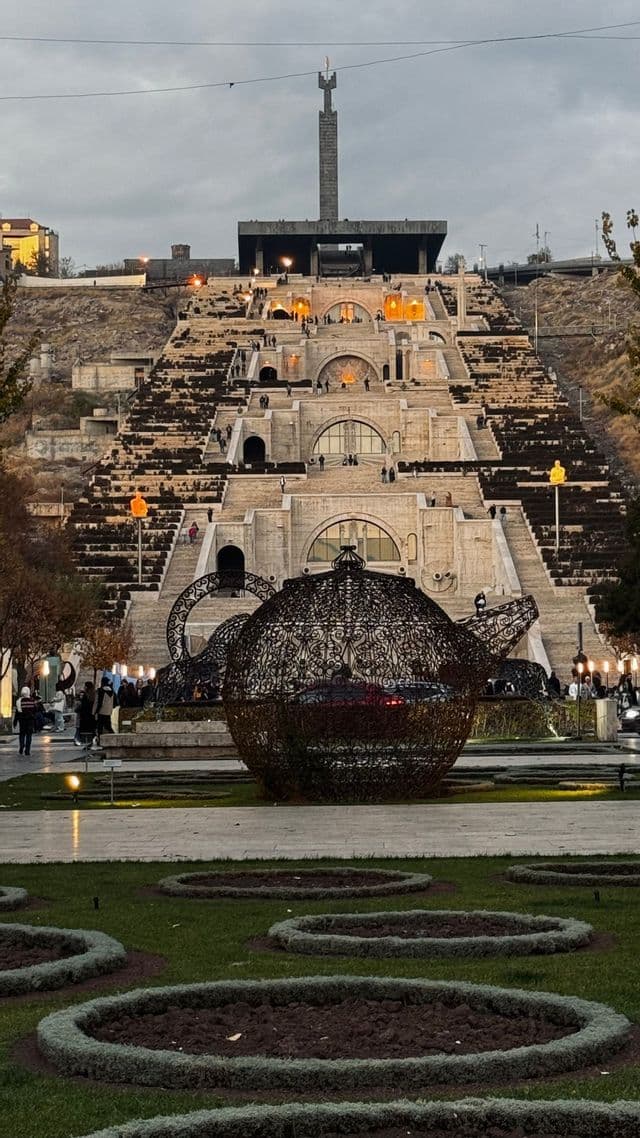 Una grande e intricata scultura a forma di teiera si erge in un parco di fronte a una massiccia scalinata in pietra a terrazze con un monumento in cima.
