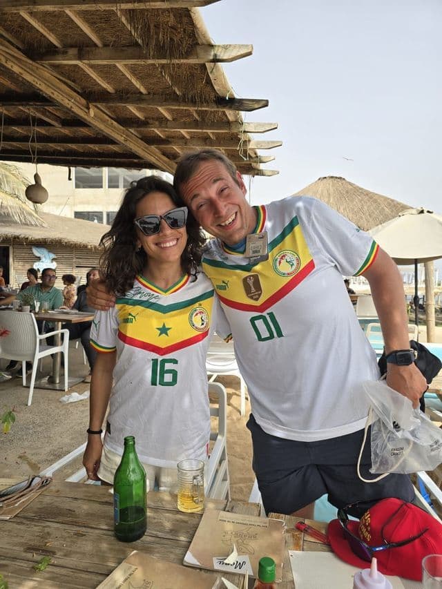 Un uomo e una donna che indossano maglie da calcio abbinate del Senegal sorridono per una foto a un tavolo in un ristorante all'aperto.