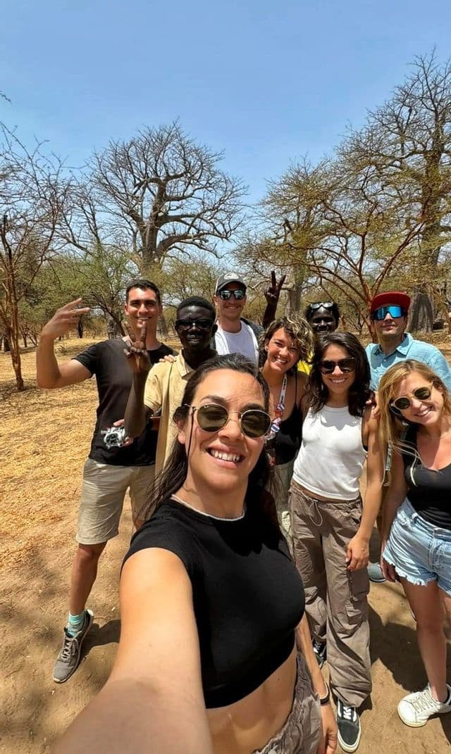 Un gruppo WeRoad in viaggio si scatta un selfie sorridente all'aperto, tra frondosi alberi di baobab, in una giornata di sole.