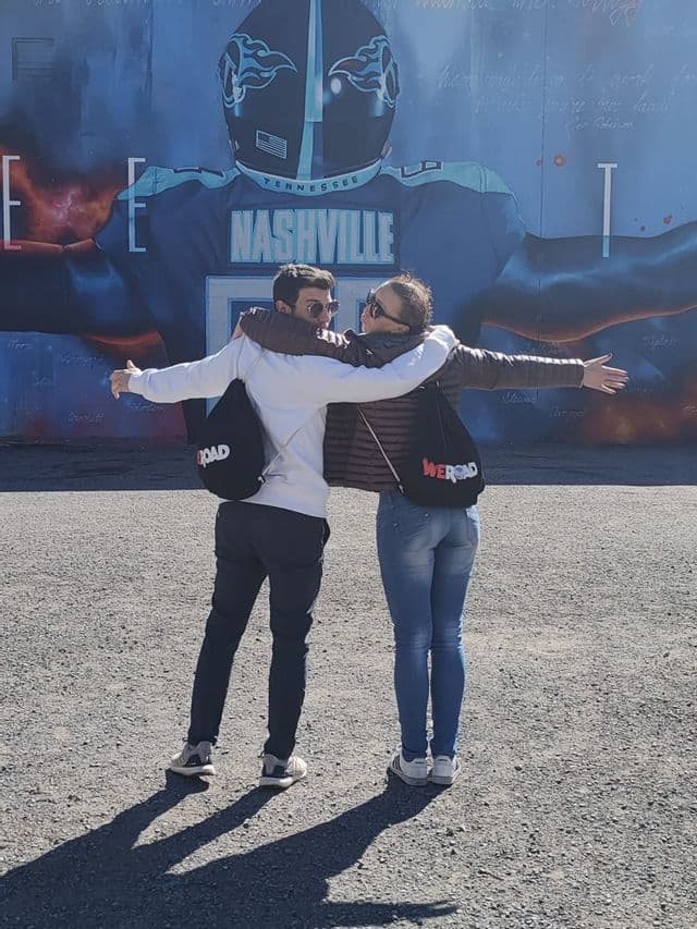Un homme et une femme d'un voyage de groupe WeRoad s'embrassent les bras tendus devant une grande fresque murale de football à Nashville.