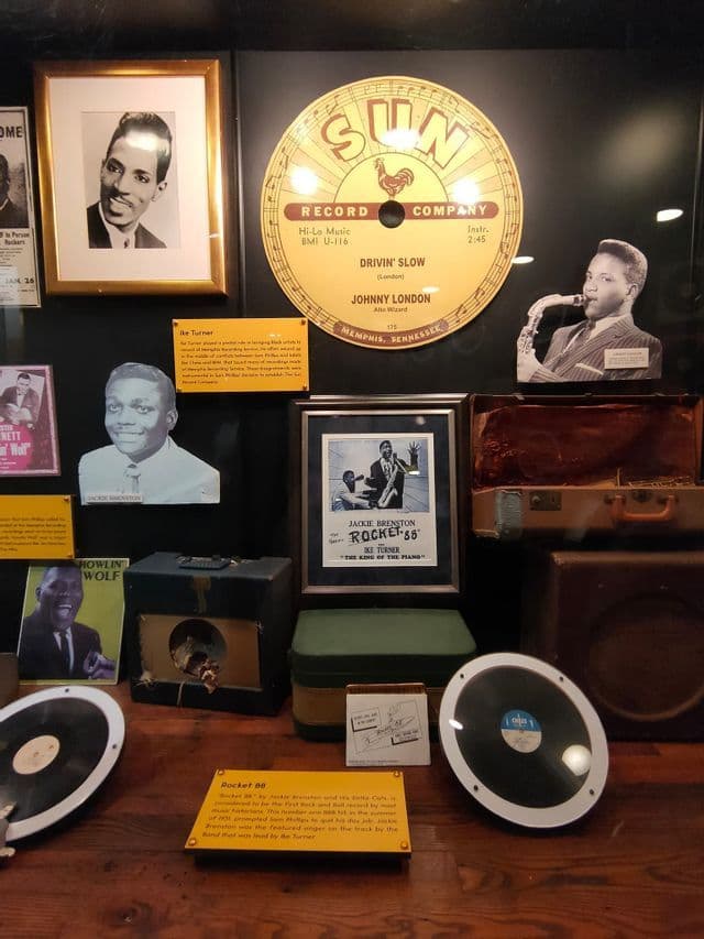 Une exposition muséale d'objets de collection de Sun Record Company, incluant des disques vintage, des photos d'artistes et de vieux amplificateurs.
