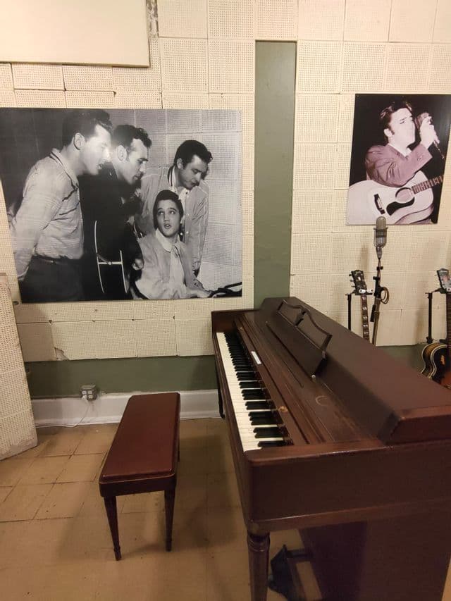 Un studio de musique avec un piano droit, un banc, des microphones vintage et de grandes photographies d'Elvis Presley au mur.