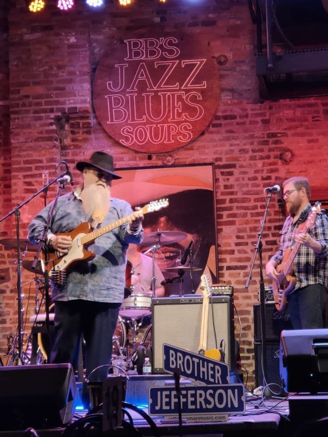 La band Brother Jefferson si esibisce dal vivo sul palco al club BB's Jazz Blues Soups, davanti a un muro di mattoni.