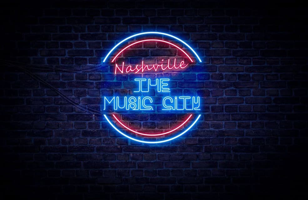 Un'insegna al neon rossa e blu con la scritta 'Nashville The Music City' che brilla su un muro di mattoni scuri.