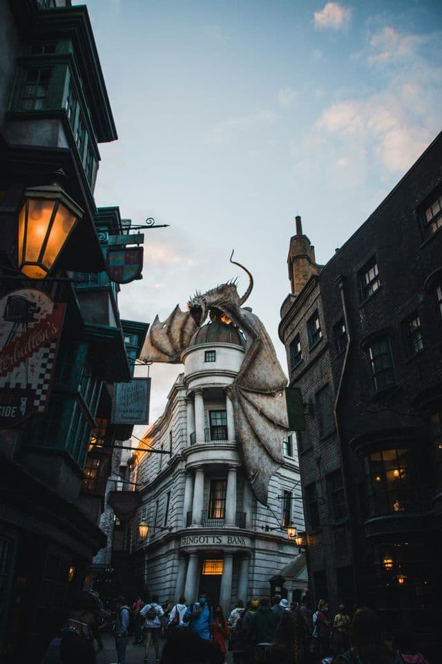 Una vista dal basso di una grande statua di drago appollaiata in cima all'edificio a cupola della Banca Gringotts su una strada affollata e all'antica.
