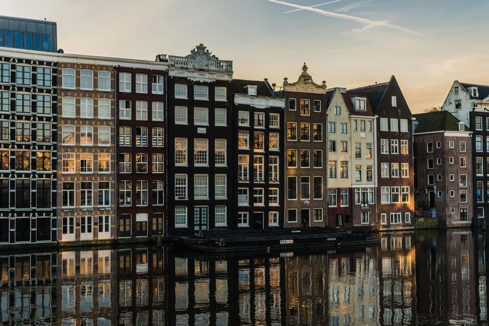 Une rangée de maisons traditionnelles au bord du canal se reflétant dans l'eau pendant un coucher de soleil chaud.