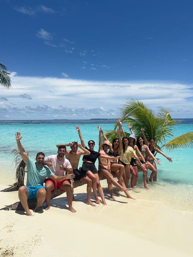 Un grupo de WeRoad posando juntos en una palmera inclinada en una playa de arena blanca con agua turquesa.
