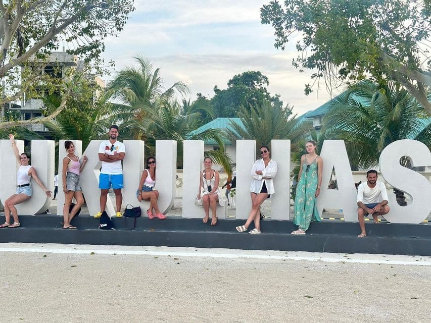 Un viaje en grupo de WeRoad posa para una foto alrededor de grandes letras blancas que forman UKULHAS, con palmeras de fondo.