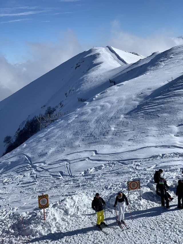 Un viaggio di gruppo WeRoad sugli sci su un pendio innevato sotto un cielo azzurro e soleggiato.