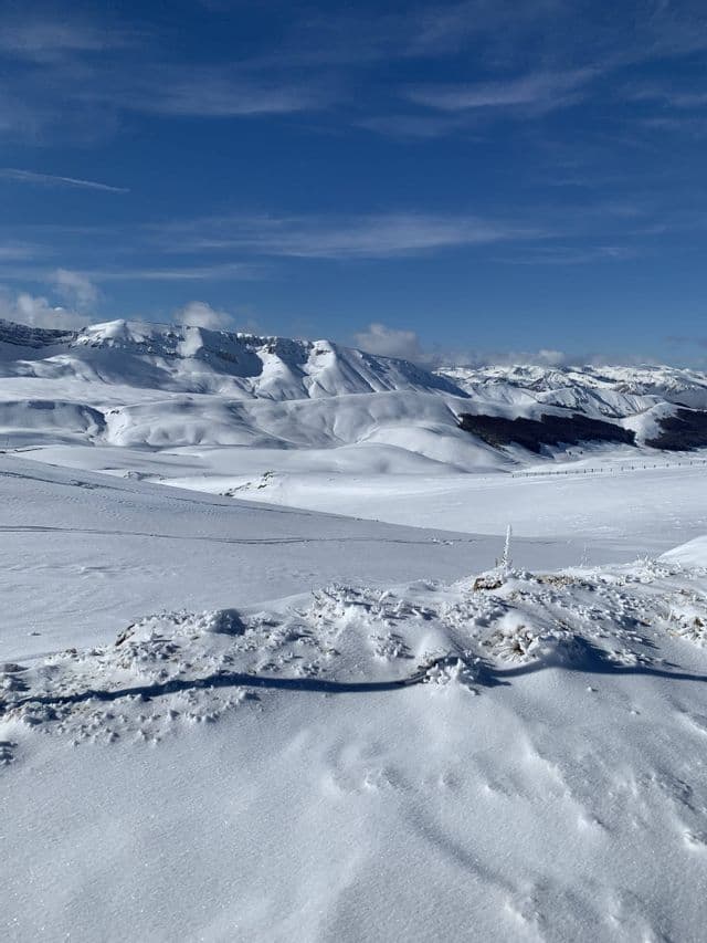Un'ampia valle innevata conduce a una catena di montagne innevate sotto un cielo azzurro e terso.