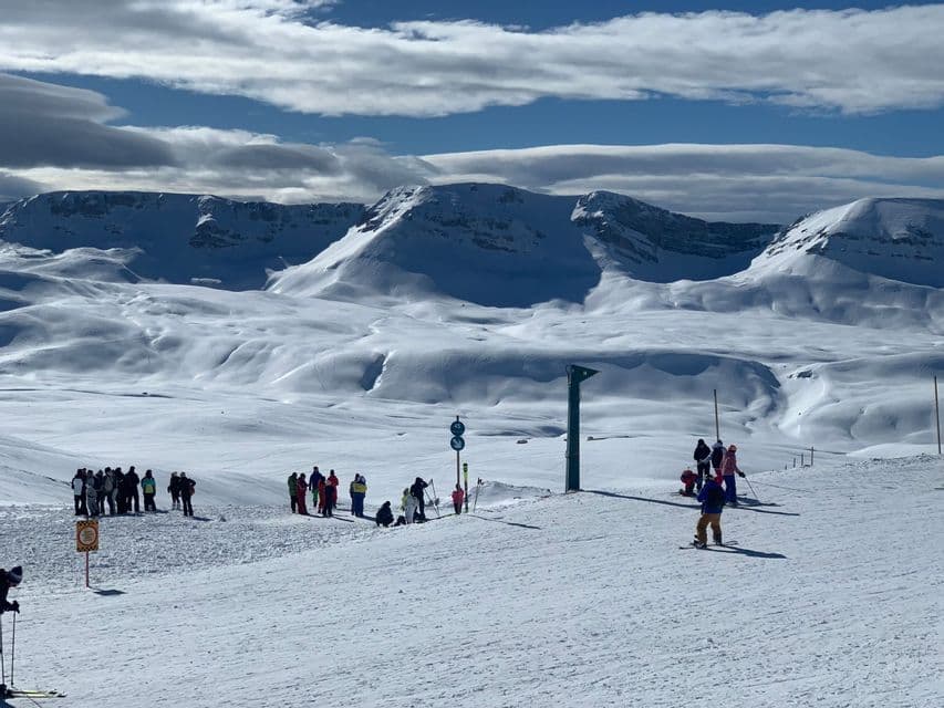 Un viaggio di gruppo WeRoad di sciatori e snowboarder su un pendio innevato, con una vasta catena montuosa sullo sfondo.