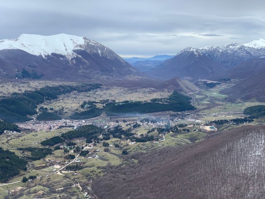 Una vista dall'alto di una città incastonata in una valle verde circondata da grandi montagne innevate sotto un cielo nuvoloso