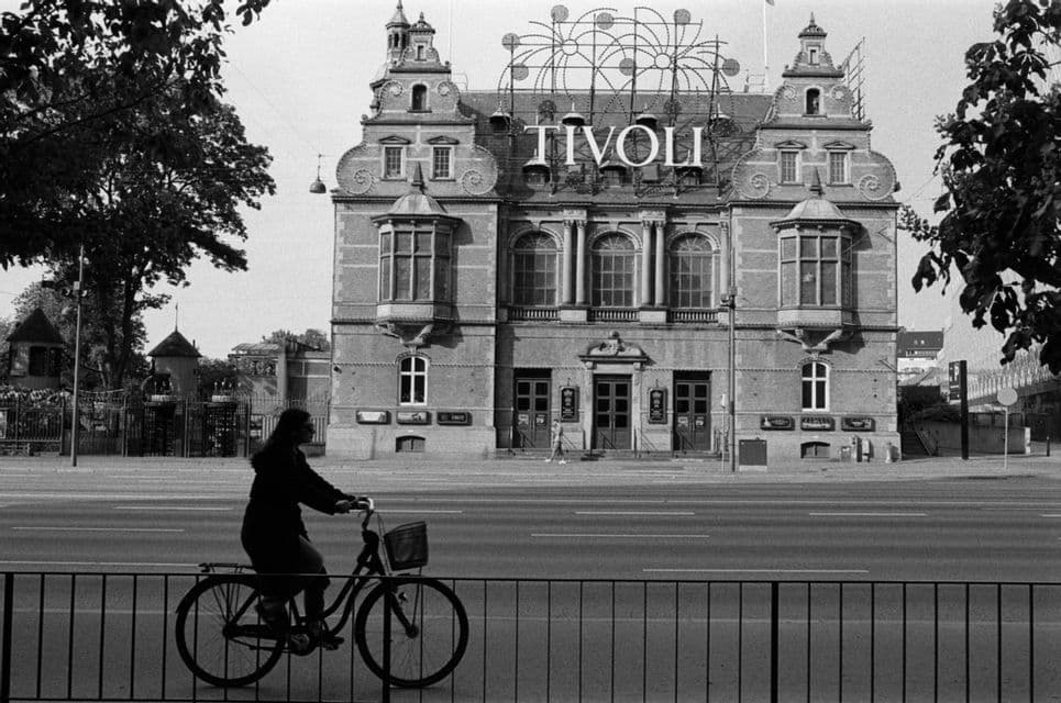 A person on a bicycle rides past the ornate Tivoli building in this black and white photograph.