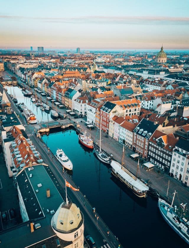 Aerial view of a city canal lined with colorful buildings and boats, with a Danish flag on a dome in the foreground.