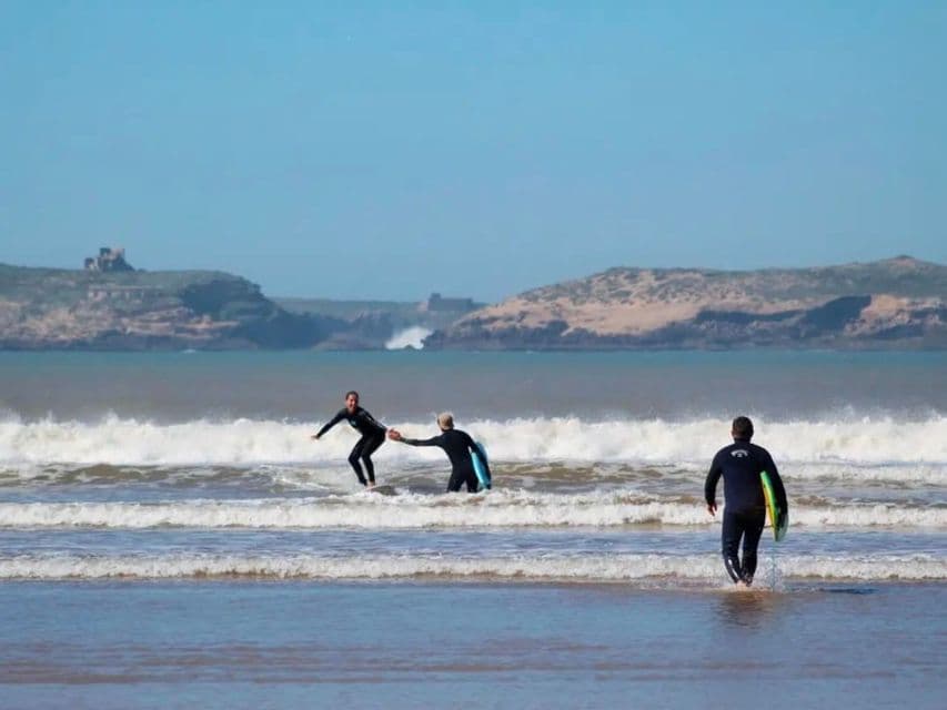 Eine WeRoad Gruppenreise zum Surfenlernen im Meer: Eine Person reitet eine Welle, während eine andere hilft.