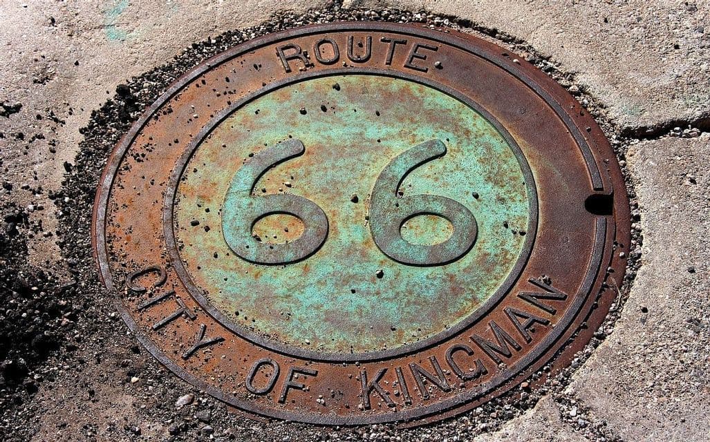 Un primer plano de una placa de metal oxidada en una acera, con 'Ruta 66' y 'Ciudad de Kingman' grabadas en ella.