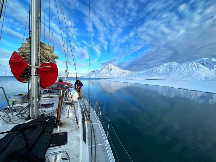 Vista dal ponte di una barca a vela durante un viaggio di gruppo WeRoad, navigando in acque calme accanto a montagne innevate e ghiaccio.