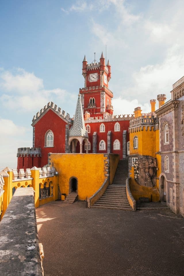 Un castello dai colori vivaci, dipinto di rosso e giallo, con una torre dell'orologio e un cortile con scale in pietra.