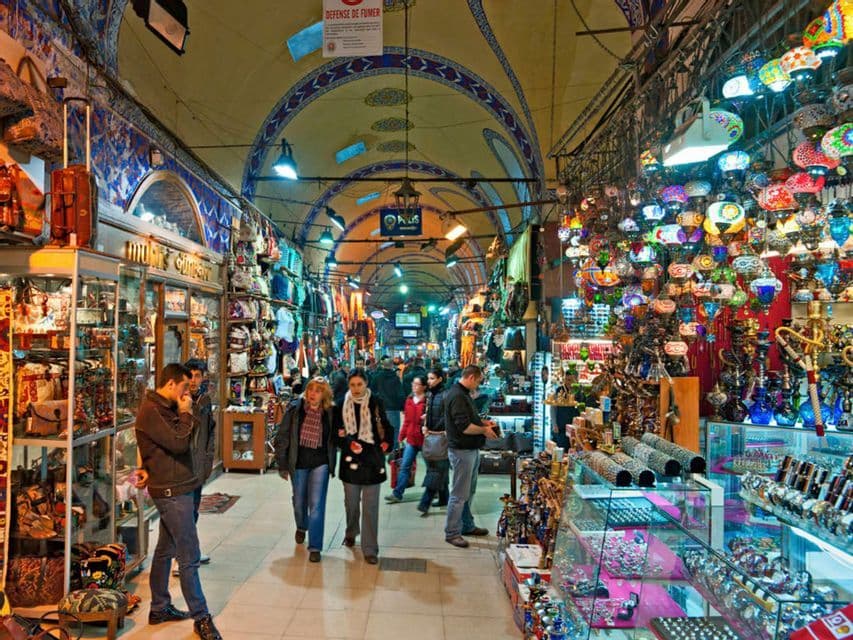 Le persone camminano attraverso un vivace mercato coperto, con negozi che vendono lanterne colorate, gioielli e borse sotto un soffitto ad arco.