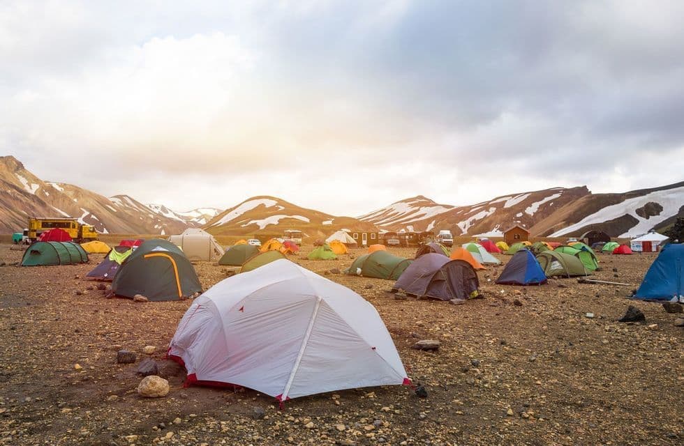 Colorful tents pitched on rocky ground at a large campsite with snow-capped mountains in the background.