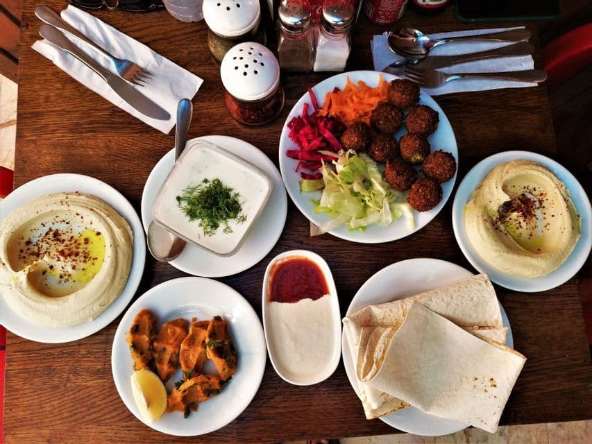 Vista cenital de una comida extendida sobre una mesa de madera, con falafel, hummus, pan de pita, ensaladas y salsas.