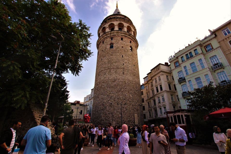 Una multitud se congrega al pie de una histórica torre de piedra en una plaza de la ciudad.