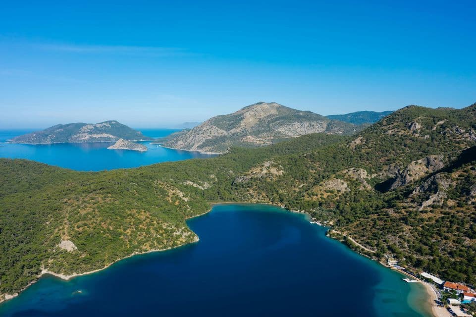Veduta aerea di una profonda baia blu, circondata da verdi colline e isole alberate sotto un cielo limpido.