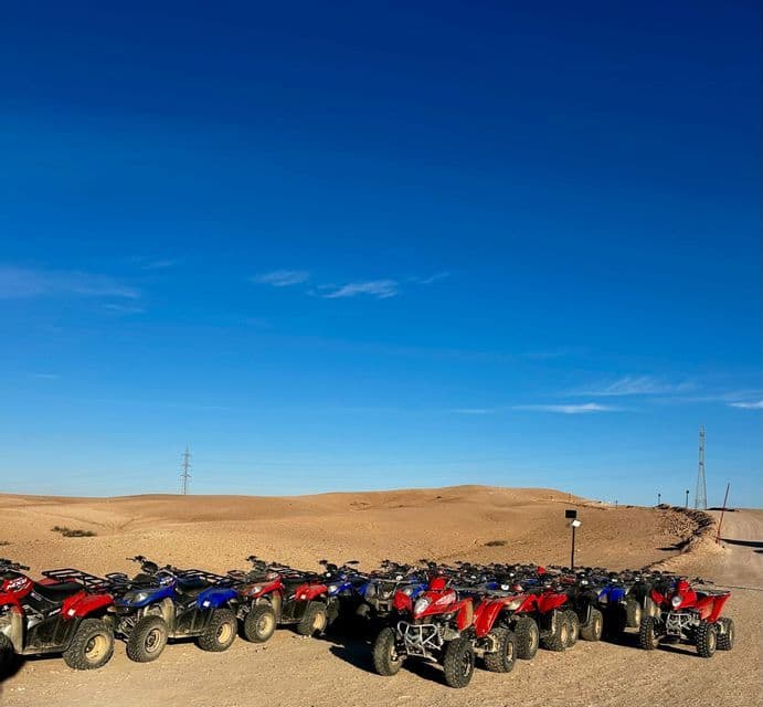 Quads rojos y azules estacionados en fila en el desierto, con dunas de arena bajo un cielo despejado.