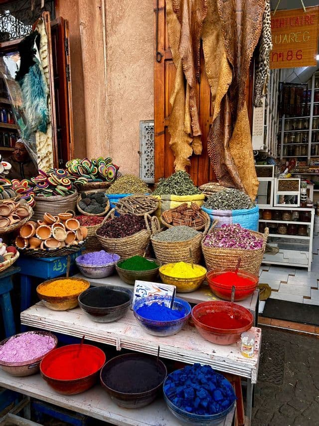 Pigmentos en polvo de colores en cuencos y especias variadas en cestas de mimbre están a la venta en un puesto de mercado al aire libre.