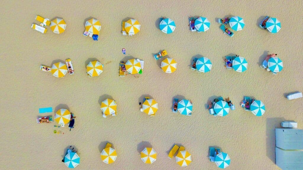 Una vista aerea, dall'alto, di ombrelloni gialli e turchesi disposti in file ordinate su una spiaggia sabbiosa con persone che si rilassano.