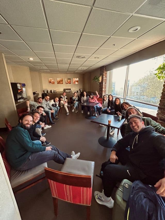 Un gruppo WeRoad in viaggio è seduto in cerchio in una sala comune d'albergo, in posa e sorridente per una foto di gruppo.