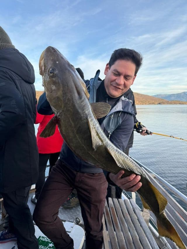 Un hombre en un viaje en grupo de WeRoad sonríe mientras sostiene un gran pez recién pescado en la cubierta de un barco.