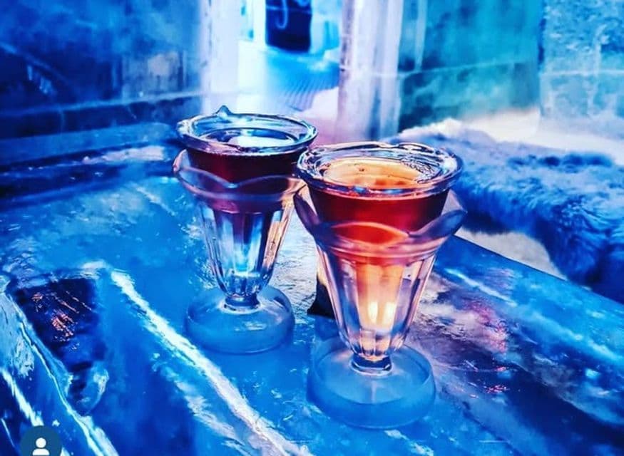 Dos chupitos tallados en hielo y llenos de una bebida roja, sobre una barra de hielo.