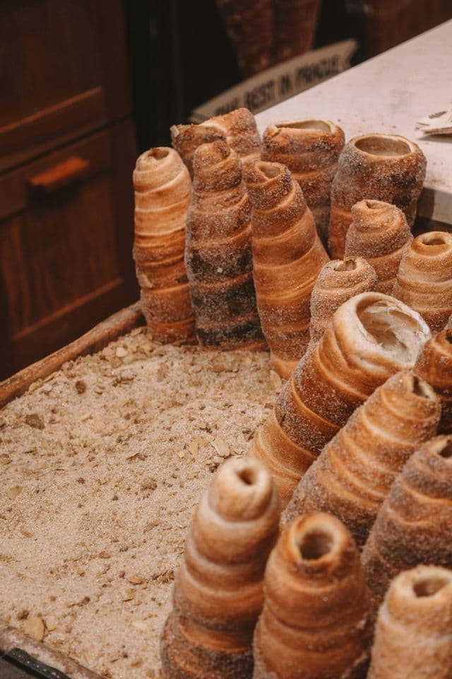 A close-up of several cone-shaped pastries, Trdelník, coated in sugar and standing upright in a display tray.