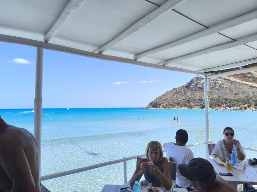 Un viaje en grupo de WeRoad almorzando en una terraza cubierta con vistas a un mar turquesa y una costa montañosa.